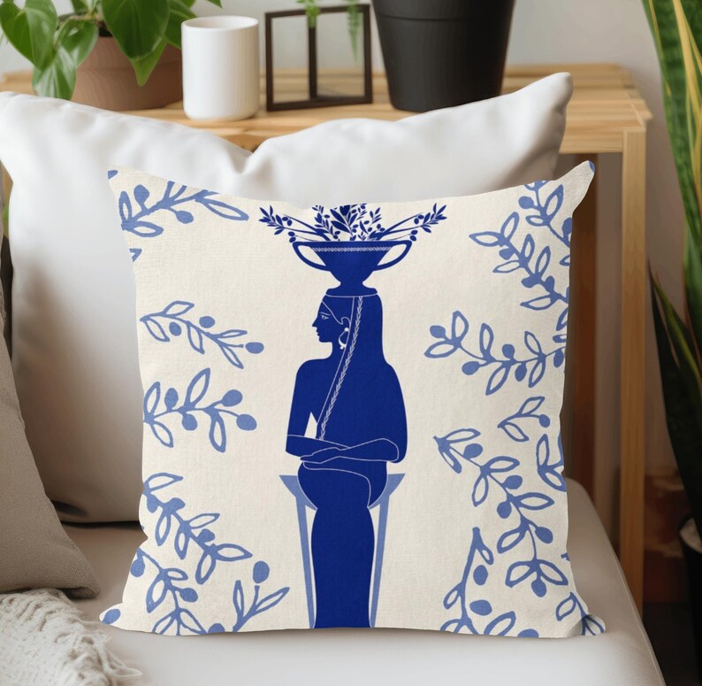 Puede incluir: Coj&iacute;n decorativo con una silueta azul de una persona que lleva un cuenco de flores. El fondo crema est&aacute; adornado con motivos florales azules. Un elemento decorativo para el sal&oacute;n o el dormitorio.