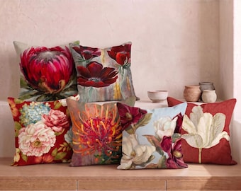 May include: A collection of six square throw pillows featuring vibrant floral prints. The designs include a large pink protea, deep red poppies, a bouquet of pink and blue peonies, an orange pincushion flower, white magnolias, and a single white tulip.