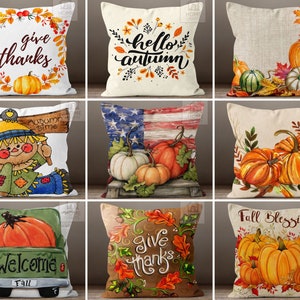 May include: A collection of decorative throw pillows with autumn-themed designs. Pillows feature pumpkins, fall leaves, and phrases like "Give Thanks," "Hello Autumn," and "Fall Blessings." The color palette includes orange, brown, and green.