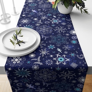 May include: A navy blue table runner with a white snowflake pattern. The runner is decorated with snowflakes of various sizes and styles, as well as small stars.