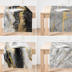 May include: Four table runners with marble designs. Each runner features a different color scheme, including black, white, gray, and gold. The runners are rectangular and placed on a wooden table, with plates and glasses.