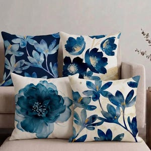 May include: A set of four square throw pillows featuring blue and white floral patterns. One pillow has a dark blue background with light blue flowers, while the others feature watercolor-style blue blossoms on white or cream-colored backgrounds.