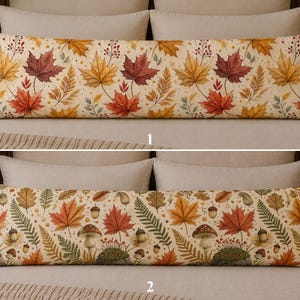 May include: Two long rectangular body pillows featuring autumn-themed patterns. The top pillow displays a print of orange, red, and yellow maple leaves with small berries. The bottom pillow shows a pattern of mushrooms, acorns, and ferns.