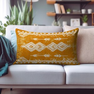 May include: Mustard yellow rectangular pillow with a white tribal pattern. The design includes arrows, diamonds, and geometric shapes. The pillow is on a gray couch, with other pillows and decor in the background.