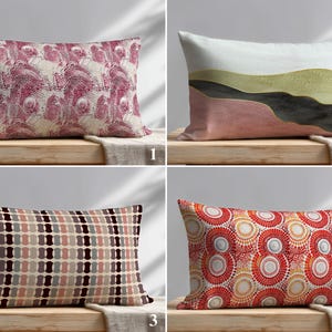 Könnte beinhalten: Vier dekorative rechteckige Kissen mit verschiedenen Mustern. Die Muster umfassen ein florales Design in Rosa, eine abstrakte Landschaft, ein geometrisches Muster in Braun und Grau sowie ein kreisförmiges Muster in Rot und Orange.