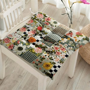 Könnte beinhalten: Ein Stuhlkissen mit floralem Muster und Patchwork-Design in Grün-, Schwarz-, Weiß- und Rosatönen. Das Kissen ist aus Stoff und hat eine gesteppte Textur.