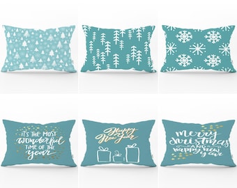 May include: A set of six rectangular throw pillows in teal and white. Designs include white pine trees, snowflakes, and gold text reading It's the most wonderful time of the year, Happy New Year, and Merry Christmas and happy new year.