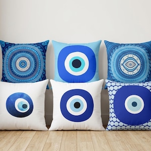 May include: A set of six square throw pillows featuring various blue and white evil eye designs. The patterns include concentric circles, watercolor effects, and geometric motifs in shades of navy, royal blue, light blue, and white.