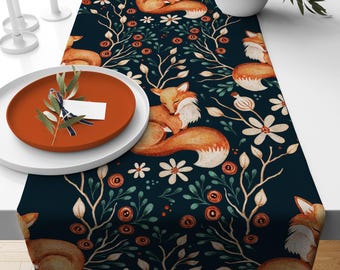 May include: A dark blue table runner with a repeating pattern of sleeping foxes, white flowers, and floral elements. The foxes are orange and white, and the flowers are white. The runner is on a white table with a plate.