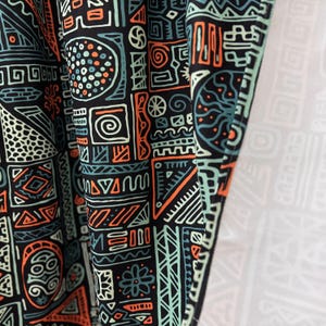 May include: Black fabric with a geometric pattern in orange, green, and white. The pattern is made up of various shapes, including circles, squares, triangles, and lines.
