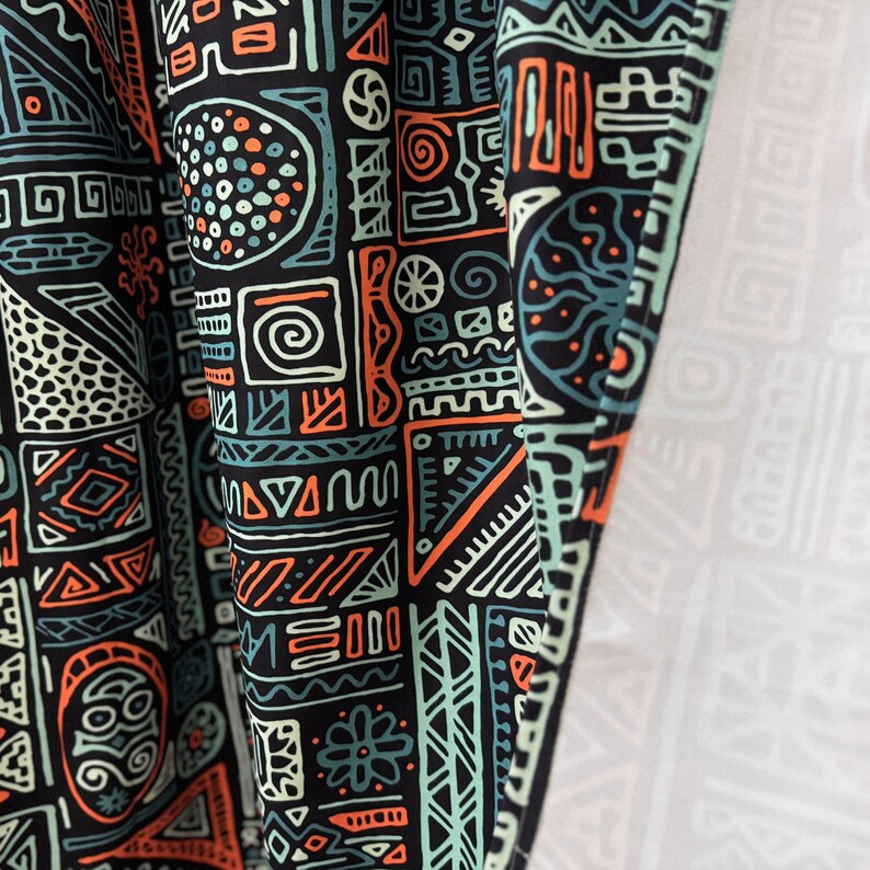 May include: Black fabric with a geometric pattern in orange, green, and white. The pattern is made up of various shapes, including circles, squares, triangles, and lines.