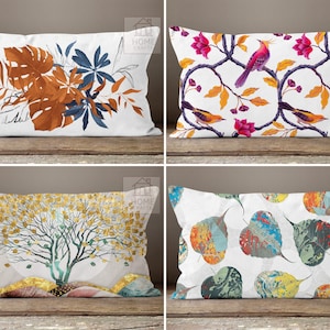 May include: Four rectangular throw pillows with nature-themed designs. One pillow features brown and blue leaves, another has birds and flowers, a third displays a golden tree, and the last showcases colorful leaf patterns. All pillows are on a wooden surface.