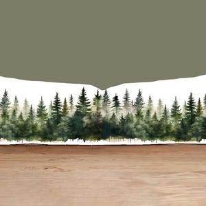 May include: A rectangular decorative pillow featuring a watercolor painting of a forest scene. The artwork depicts a line of evergreen trees in varying shades of green, with a misty background. The pillow is on a wooden surface.