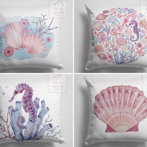 Pode incluir: Conjunto de quatro capas de almofada decorativas com ilustrações de aquarela de conchas, corais e cavalos-marinhos. As capas de almofada são brancas com um fundo azul claro e o texto "HOME CRAFTS" no canto superior direito.