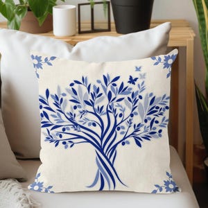 Puede incluir: Coj&iacute;n crema con un dise&ntilde;o de &aacute;rbol azul. El &aacute;rbol tiene una ilustraci&oacute;n detallada de hojas, aceitunas y una mariposa. El coj&iacute;n tiene detalles florales azules en las esquinas. Este coj&iacute;n decorativo es perfecto para a&ntilde;adir un toque de naturaleza a cualquier habitaci&oacute;n.