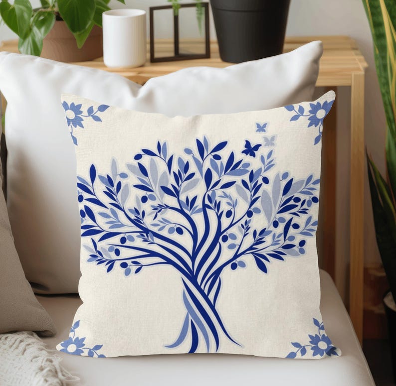 Puede incluir: Coj&iacute;n crema con un dise&ntilde;o de &aacute;rbol azul. El &aacute;rbol tiene una ilustraci&oacute;n detallada de hojas, aceitunas y una mariposa. El coj&iacute;n tiene detalles florales azules en las esquinas. Este coj&iacute;n decorativo es perfecto para a&ntilde;adir un toque de naturaleza a cualquier habitaci&oacute;n.