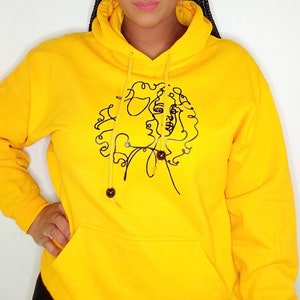 May include: Yellow hoodie with a black line drawing of a woman's face on the front.