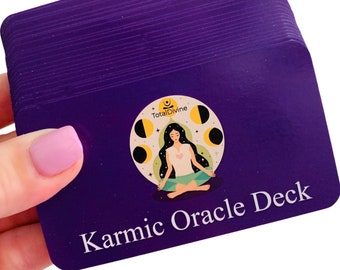 Pode incluir: Um baralho de cartas retangulares roxas com um gráfico circular central de uma pessoa meditando cercada por fases da lua. O texto TotalDivine aparece acima da figura e as palavras Karmic Oracle Deck estão impressas em branco na base.