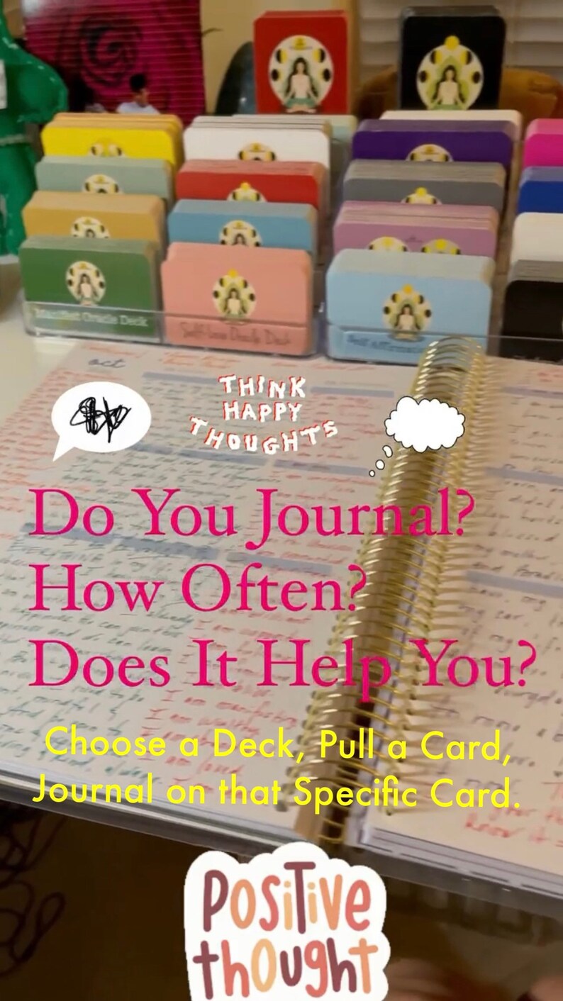 May include: A close-up of an open journal with the text "Do You Journal? How Often? Does It Help You? Choose a Deck, Pull a Card, Journal on that Specific Card." written in pink. The journal has gold rings and is lying on a table with a stack of colorful card decks in the background. The text "Think Happy Thoughts" is written in white on a pink card deck. A sticker with the text "Positive thought" is in the foreground.