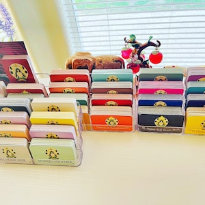 May include: A collection of colorful oracle card decks organized in clear plastic holders. The decks are labeled with their names, including "My Higher Self Oracle Deck", "Twin Flame Oracle Deck", "Archangel Oracle Deck", and "Full Moon Oracle Deck".