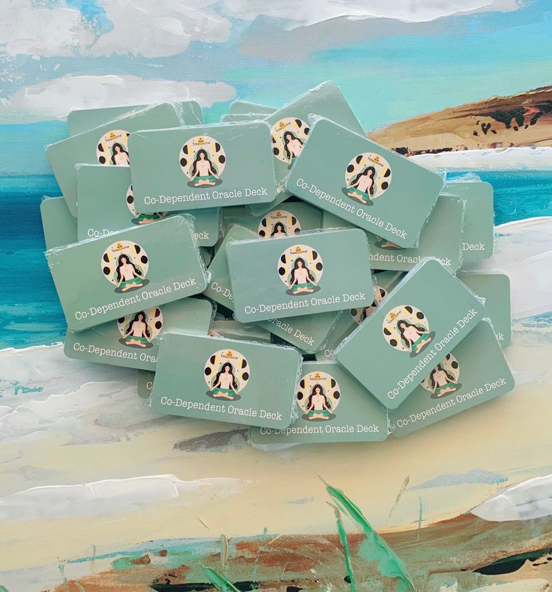 May include: A stack of teal blue cards with the text "Co-Dependent Oracle Deck" printed on each card. The cards feature a stylized illustration of a person sitting in a meditative pose.