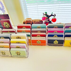 May include: A collection of colorful oracle decks organized in clear plastic holders. The decks are labeled with their names, including "My Higher Self Oracle Deck", "Twin Flame Oracle Deck", "Archangel Oracle Deck", and "Full Moon Oracle Deck".