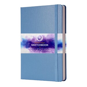 Puede incluir: Un cuaderno de bocetos azul claro con cierre el&aacute;stico. La portada tiene una banda blanca con el texto "Premium Paper SKETCHBOOK". Contiene 120 p&aacute;ginas sin &aacute;cido y mide 14,5 x 21 cm.