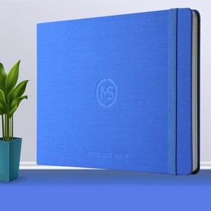 May include: A blue watercolour album with a textured cover and a blue ribbon closure. The album has a logo embossed on the front that says "MS" and the words "Watercolour Album" printed below the logo.