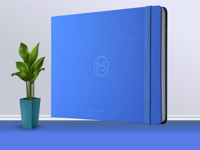 May include: A blue watercolour album with a textured cover and a blue ribbon closure. The album has a logo embossed on the front that says "MS" and the words "Watercolour Album" printed below the logo.