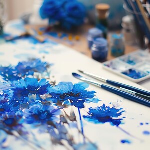May include: A watercolour painting of blue flowers on white paper. Two blue paintbrushes are lying on the paper.