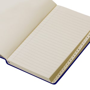 Pode incluir: Um caderno azul com um &iacute;ndice alfab&eacute;tico dourado na borda das p&aacute;ginas. O caderno tem p&aacute;ginas pautadas.