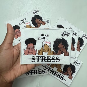 May include: Three embroidered patches with a white background and black outlines. Each patch features three women with their hands over their eyes, ears, and mouth. The text "Blah Blah" is above the women and "Stress" is below them. The patches are stacked on top of each other.