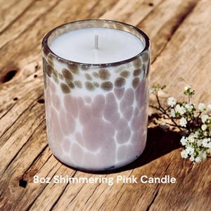 May include: An 8 oz candle in a clear glass jar with a shimmering pink and brown speckled design. The candle is unlit and has a white wax top.