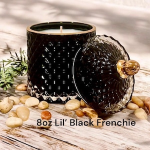 May include: Black glass candle jar with a gold lid and a white candle inside. The jar has a diamond pattern and the lid has a gold knob. The candle is labeled "8oz Lil' Black Frenchie".
