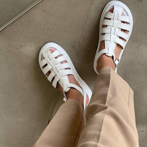 May include: White leather platform sandals with a caged design. The sandals have a buckle closure at the ankle.