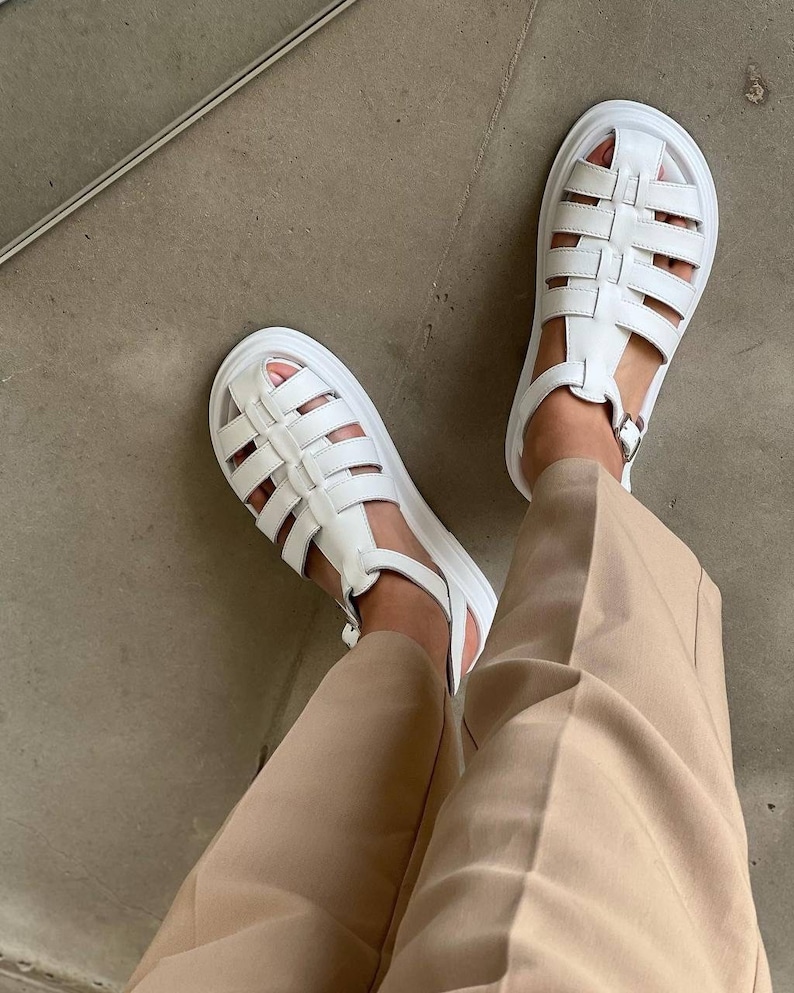 May include: White leather platform sandals with a caged design. The sandals have a buckle closure at the ankle.
