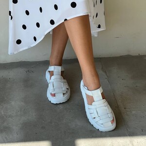 May include: White leather sandals with a chunky platform sole and a woven strap design.