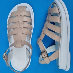 May include: A pair of beige leather sandals with white platform soles. The sandals have a woven design and buckle closures.