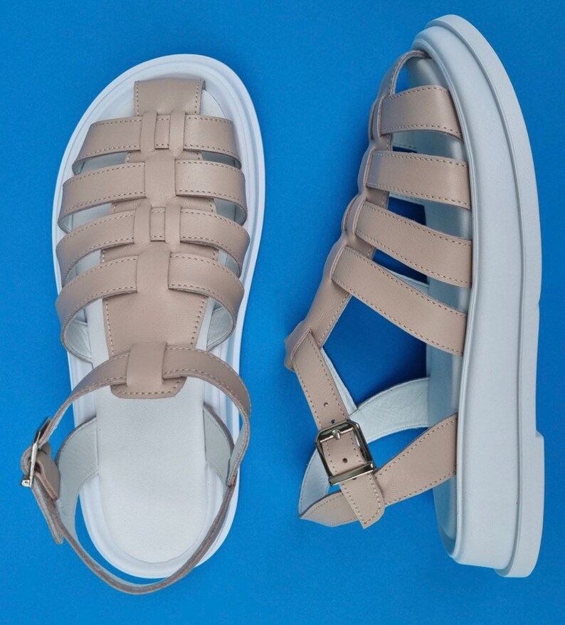 May include: A pair of beige leather sandals with white platform soles. The sandals have a woven design and buckle closures.