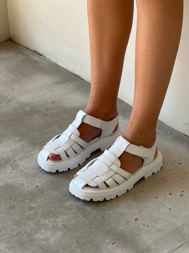 May include: White leather sandals with a chunky platform sole and a caged design. The sandals have a velcro strap closure.