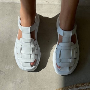 May include: White leather sandals with a chunky platform sole and a woven strap design.