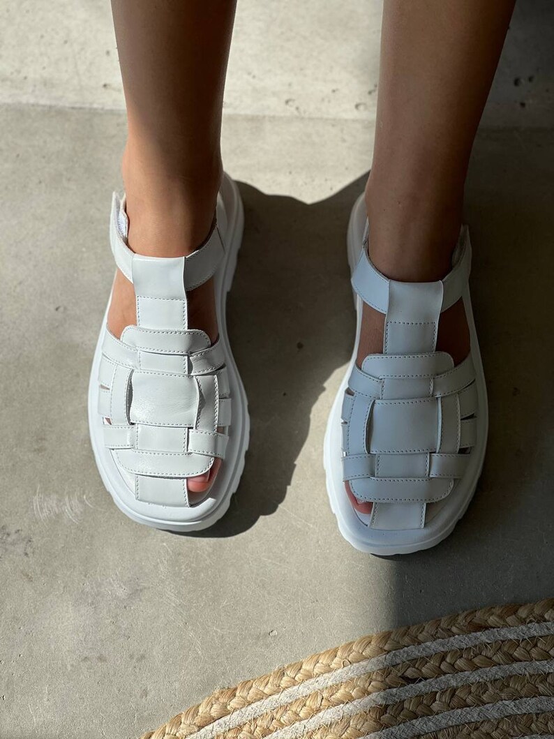 May include: White leather sandals with a chunky platform sole and a woven strap design.