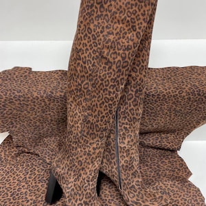 May include: A pair of brown suede over-the-knee boots with a leopard print pattern. The boots have a block heel and a pointed toe.