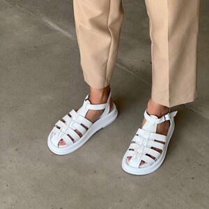 May include: White leather sandals with a chunky platform sole and a criss-cross strap design.