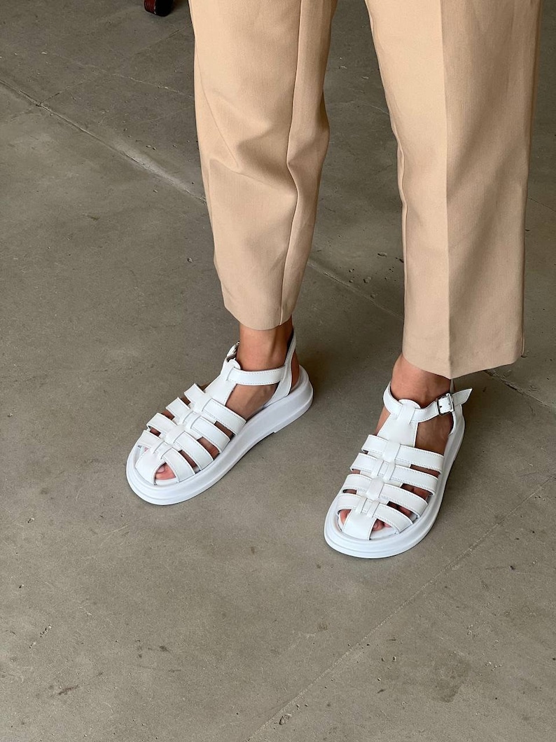 May include: White leather sandals with a chunky platform sole and a criss-cross strap design.