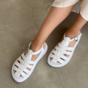 May include: White leather sandals with a chunky platform sole and a cage-like design. The sandals have a buckle closure at the ankle.