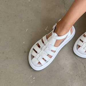 May include: White leather sandals with a chunky platform sole and a cage-like design. The sandals have a buckle closure at the ankle.