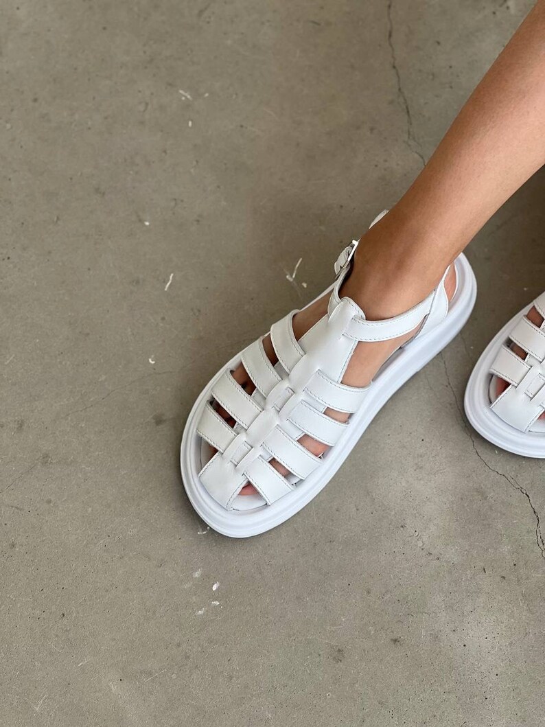 May include: White leather sandals with a chunky platform sole and a cage-like design. The sandals have a buckle closure at the ankle.