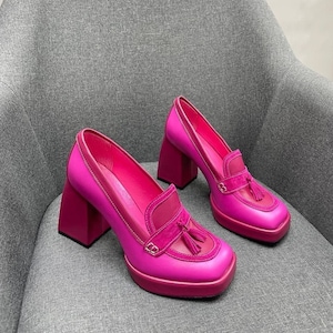 May include: A pair of bright pink platform heels with a chunky block heel and a tassel detail. The shoes have a square toe and a suede-like finish.