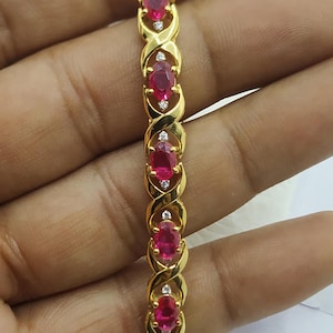 Puede incluir: Una pulsera de oro con un diseño de entrelazado con piedras preciosas de rubí ovaladas y pequeños diamantes transparentes.